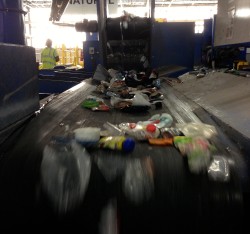 Recyclable plastics tumble down a conveyor belt at an area Materials Recovery Facility (MRF) for sorting.